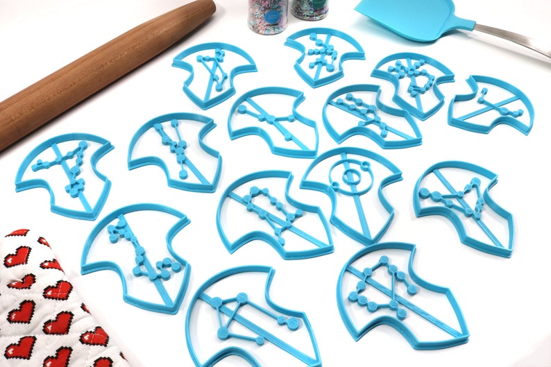 Puede incluir: Un juego de 13 cortadores de galletas de pl&aacute;stico azul con forma de constelaciones. Los cortadores est&aacute;n dispuestos sobre una superficie blanca.