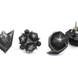 May include: Four silver-colored earrings with geometric designs. The earrings are in the shape of a triangle, a sphere, a crescent moon, and a swirl.