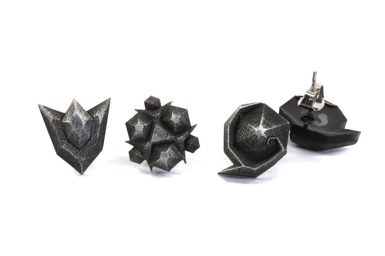 May include: Four silver-colored earrings with geometric designs. The earrings are in the shape of a triangle, a sphere, a crescent moon, and a swirl.