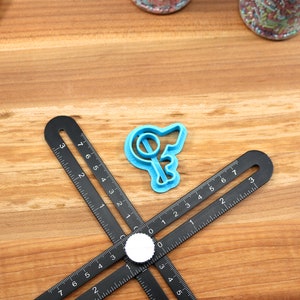 May include: A blue plastic cookie cutter shaped like a key with a circle on the top. The cutter is on a wooden surface with a black ruler.