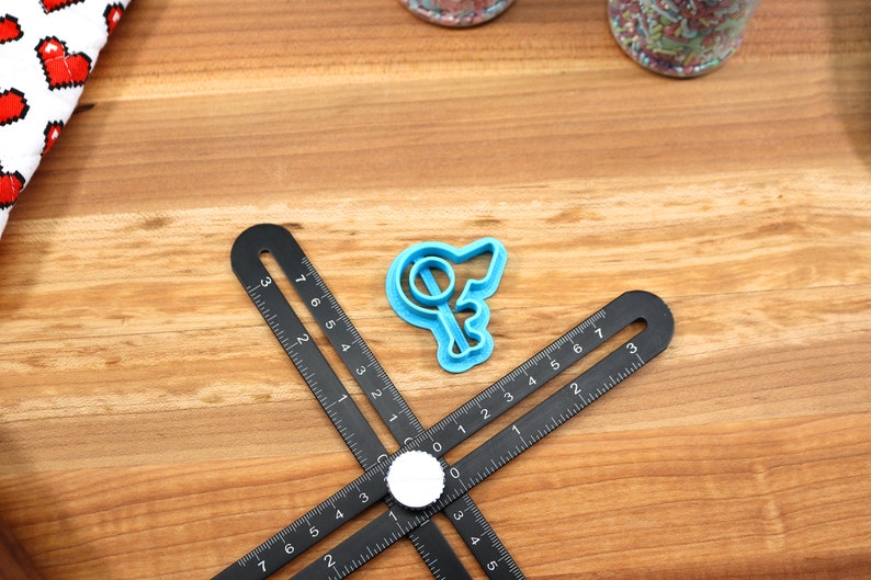 May include: A blue plastic cookie cutter shaped like a key with a circle on the top. The cutter is on a wooden surface with a black ruler.
