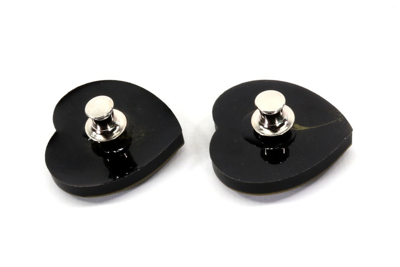 May include: Two black heart-shaped pins with silver metal clasps. The pins are shiny and have a smooth surface.