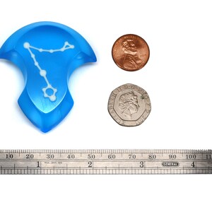 K&ouml;nnte beinhalten: Ein blauer Harz-W&uuml;rfel mit einem wei&szlig;en Sternbild-Design. Der W&uuml;rfel hat einen Durchmesser von etwa 5 cm. Der W&uuml;rfel liegt neben einem US-Penny und einer britischen M&uuml;nze zur Gr&ouml;&szlig;enbestimmung.