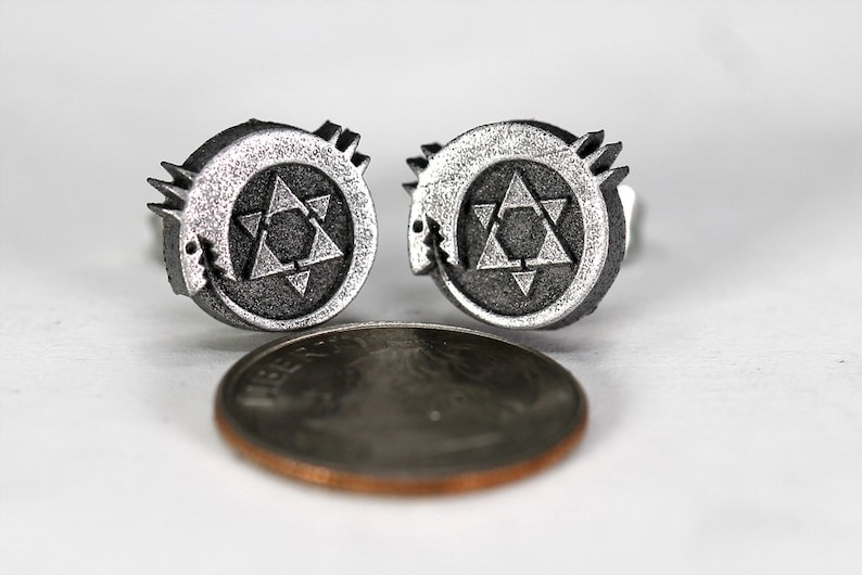 May include: A pair of silver cufflinks featuring a stylized star of David with a serpent wrapped around it. The cufflinks are about the size of a US penny.
