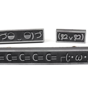 May include: Three black metal rectangular plaques with silver lettering. The top plaque reads "(づ｡◕‿‿◕｡)づ". The middle plaque reads "(♡‿♡)". The bottom plaque reads "C=C=C=C=C=┌(;・&omega;・)┐".