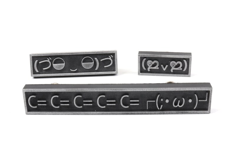 May include: Three black metal rectangular plaques with silver lettering. The top plaque reads "(づ｡◕‿‿◕｡)づ". The middle plaque reads "(♡‿♡)". The bottom plaque reads "C=C=C=C=C=┌(;・&omega;・)┐".
