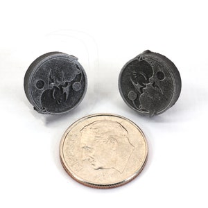 May include: Two small, round, silver-colored metal buttons with a yin-yang symbol design. The buttons are about the size of a US dime.