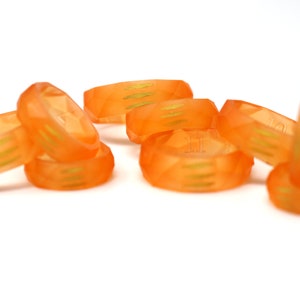 May include: A set of eight orange resin rings with a geometric design and gold accents. The rings are stacked and scattered on a white surface.