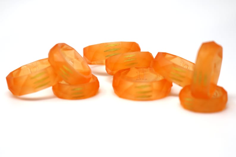 May include: A set of eight orange resin rings with a geometric design and gold accents. The rings are stacked and scattered on a white surface.