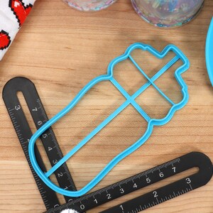 May include: A blue plastic cookie cutter shaped like a water bottle. The cutter is about 4 inches long and has a detailed design.