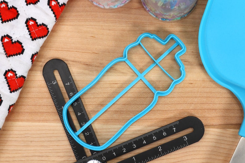 May include: A blue plastic cookie cutter shaped like a water bottle. The cutter is about 4 inches long and has a detailed design.