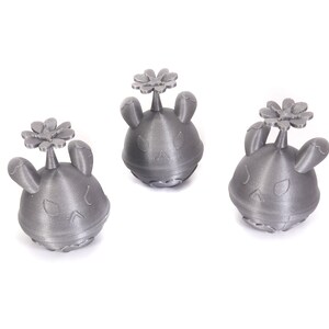 May include: Three small, gray, 3D printed figurines of a cartoon character with bunny ears and a flower on top.