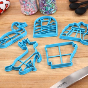 Op de afbeelding: Een set van vijf blauwe plastic koekjesvormen in de vorm van een eend, een hert, een vuurtoren, een brug en de staat Arkansas.