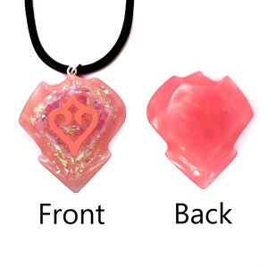 May include: Pink resin necklace with a heart-shaped pendant featuring a stylised heart design. The back of the pendant is smooth.