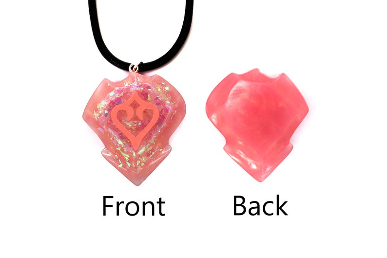May include: Pink resin necklace with a heart-shaped pendant featuring a stylised heart design. The back of the pendant is smooth.
