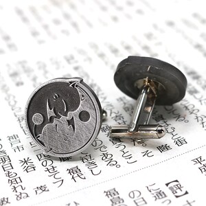 May include: A pair of silver cufflinks with a yin yang design. One cufflink features a black yin and a silver yang, while the other cufflink features a silver yin and a black yang.