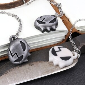 May include: Two silver necklaces with a skull-shaped pendant. One pendant is silver and the other is white.