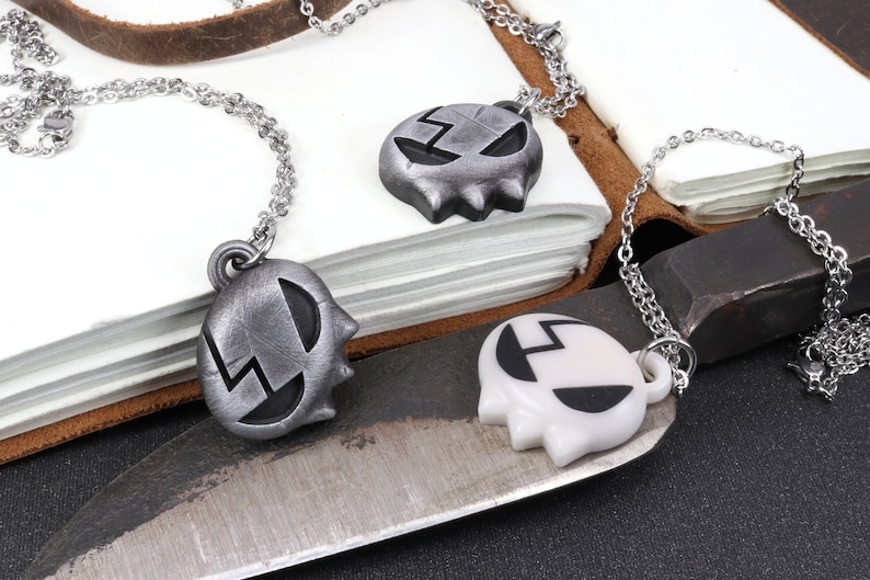 May include: Two silver necklaces with a skull-shaped pendant. One pendant is silver and the other is white.