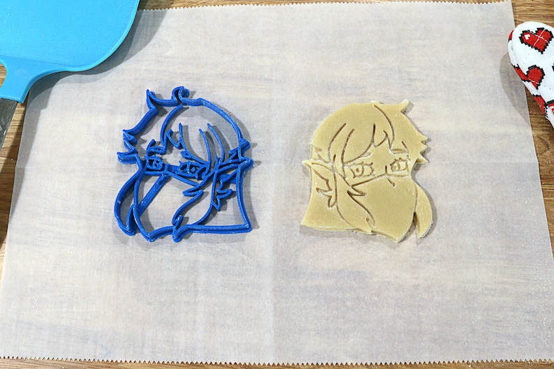 May include: Two cookie cutters, one blue and one beige, shaped like a cartoon character with short hair and a mask over their mouth and nose.