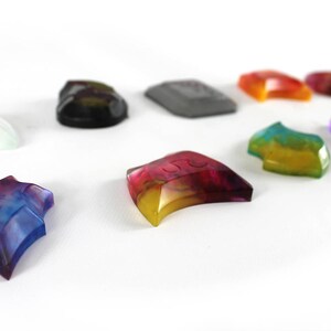 May include: Assortment of colorful, translucent, and opaque resin pieces in various shapes, including a star, crescent moon, and rectangular shapes. Some pieces have a swirl pattern, while others have a solid color.