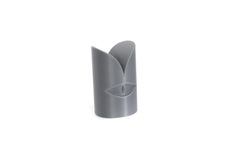 May include: A grey 3D printed candle holder with a stylised eye design.