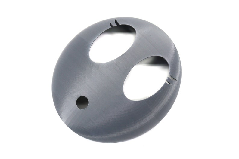 May include: A gray 3D printed model of a face mask with two large eye holes and a smaller hole in the center of the mask.