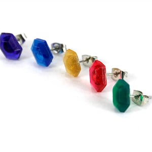 May include: Five pairs of stud earrings with different colored gemstones. The gemstones are blue, blue, yellow, red, and green.