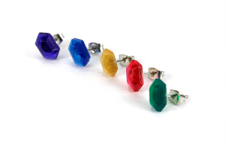 May include: Five pairs of stud earrings with different colored gemstones. The gemstones are blue, blue, yellow, red, and green.