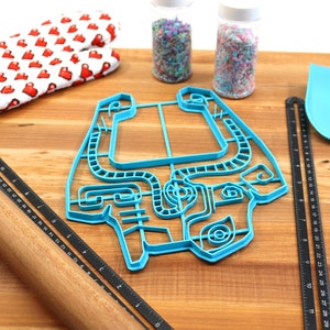 Peut inclure: Un emporte-pi&egrave;ce en plastique bleu en forme de personnage de jeu vid&eacute;o sur une planche &agrave; d&eacute;couper en bois avec un rouleau &agrave; p&acirc;tisserie, une spatule et deux pots de vermicelles.