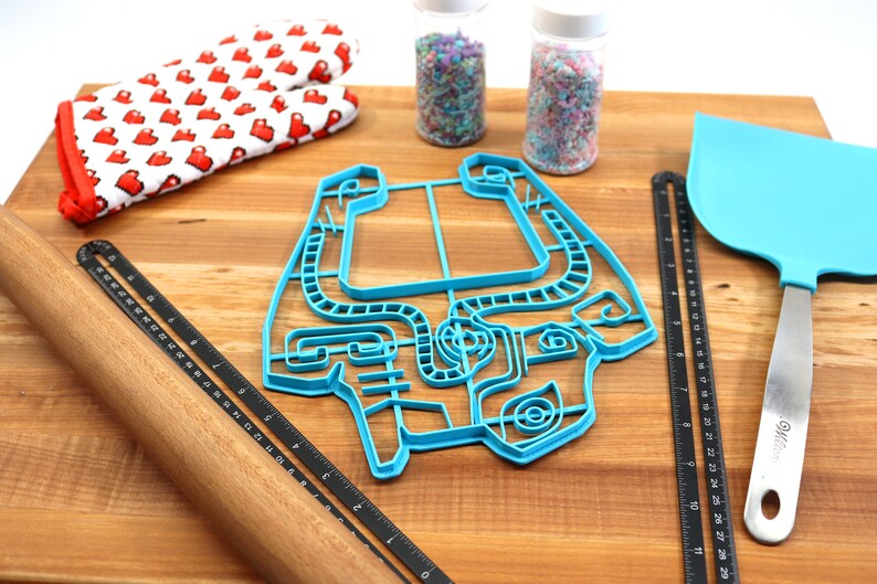 Peut inclure: Un emporte-pi&egrave;ce en plastique bleu en forme de personnage de jeu vid&eacute;o sur une planche &agrave; d&eacute;couper en bois avec un rouleau &agrave; p&acirc;tisserie, une spatule et deux pots de vermicelles.
