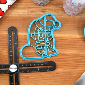 May include: Blue plastic cookie cutter shaped like a cartoon character wearing a Santa hat and holding a snowball.