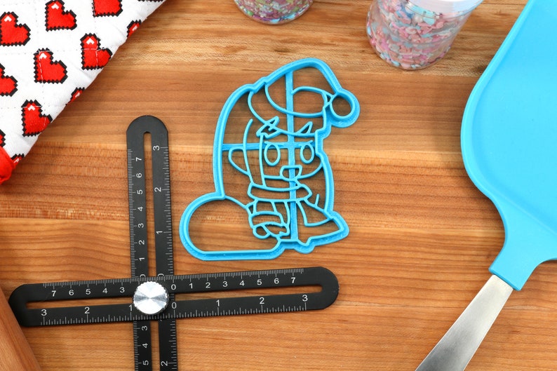 May include: Blue plastic cookie cutter shaped like a cartoon character wearing a Santa hat and holding a snowball.