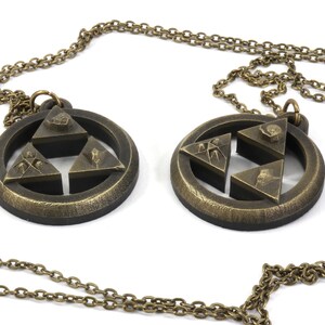Puede incluir: Dos collares de color dorado con un colgante circular que presenta un dise&ntilde;o de estrella de tres puntas. Cada colgante tiene un dise&ntilde;o diferente en cada punta de la estrella.