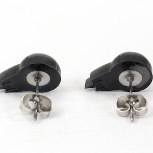 Peut inclure: Une paire de boucles d'oreilles clous en forme de cr&acirc;ne noir avec des tiges et des dos argent&eacute;s.