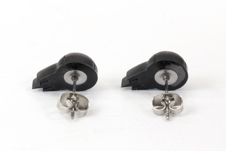 Peut inclure: Une paire de boucles d'oreilles clous en forme de cr&acirc;ne noir avec des tiges et des dos argent&eacute;s.