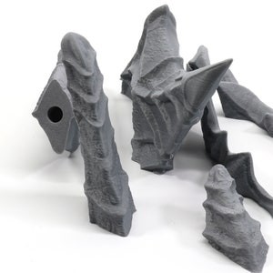 May include: Five grey 3D printed pieces of a dragon sculpture. The pieces are in various shapes and sizes, including a head, wings, and tail.