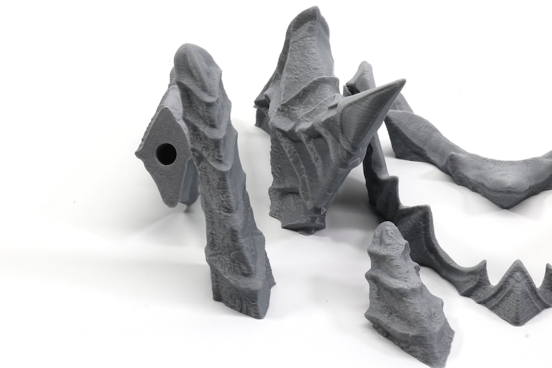 May include: Five grey 3D printed pieces of a dragon sculpture. The pieces are in various shapes and sizes, including a head, wings, and tail.