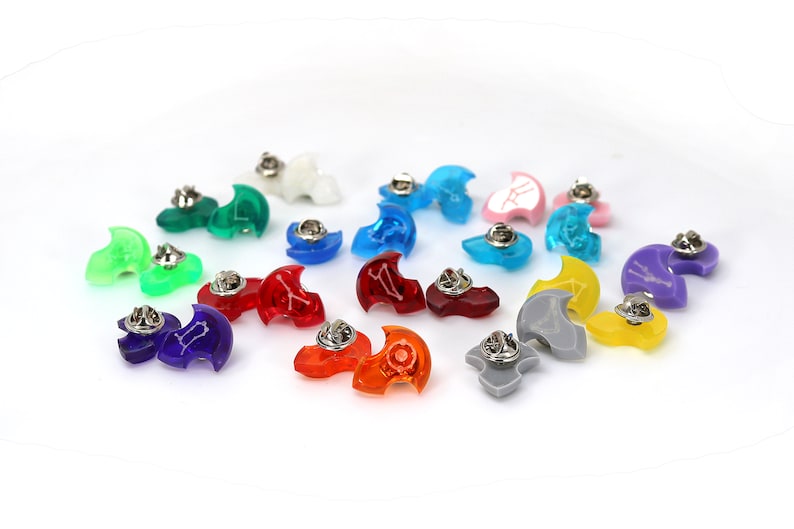 May include: A collection of 14 colorful plastic pins shaped like a crescent moon. Each pin has a different color and a different symbol on the front. The pins are arranged in a circle on a white background.