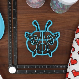 May include: A blue plastic cookie cutter shaped like a cartoon bug with large eyes and antennas.
