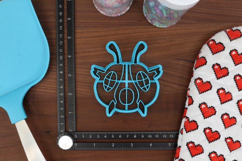 May include: A blue plastic cookie cutter shaped like a cartoon bug with large eyes and antennas.