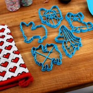 May include: A set of five blue plastic cookie cutters shaped like different breeds of dogs. The cutters are on a wooden surface.