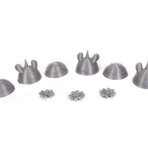 May include: A set of six gray 3D printed unicorn head figurines with a flower design. The figurines are arranged in a row on a white surface.