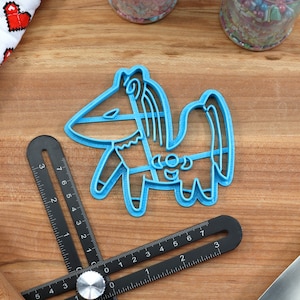 Puede incluir: Un cortador de galletas de pl&aacute;stico azul con forma de caballo de dibujos animados con melena y cola. El cortador est&aacute; sobre una superficie de madera con una regla y un rodillo.