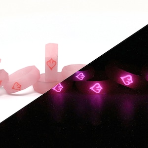May include: A set of pink glow-in-the-dark rings with a heart design. The rings are shown in both daylight and dark conditions, highlighting their glow-in-the-dark feature.