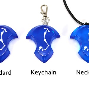 May include: Three versions of a blue pendant with a white constellation design. The pendant is available as a standard piece, a keychain, and a necklace.
