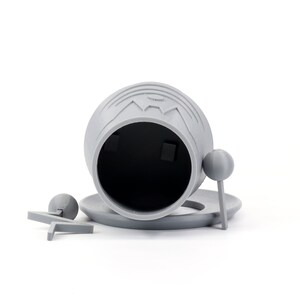 Pode incluir: Um recipiente cinzento, impresso em 3D, com a parte superior aberta, uma tampa e duas pequenas al&ccedil;as redondas. O recipiente est&aacute; sobre uma superf&iacute;cie branca.