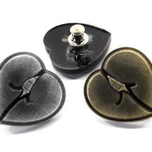 May include: Three heart-shaped metal buttons with a broken heart design. One button is black, one is silver, and one is gold.