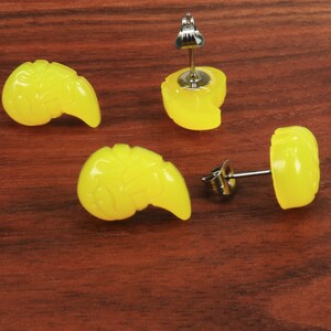 May include: Four yellow resin earrings in the shape of a stylized seashell. Two earrings have a post back and two earrings have a clip-on back.