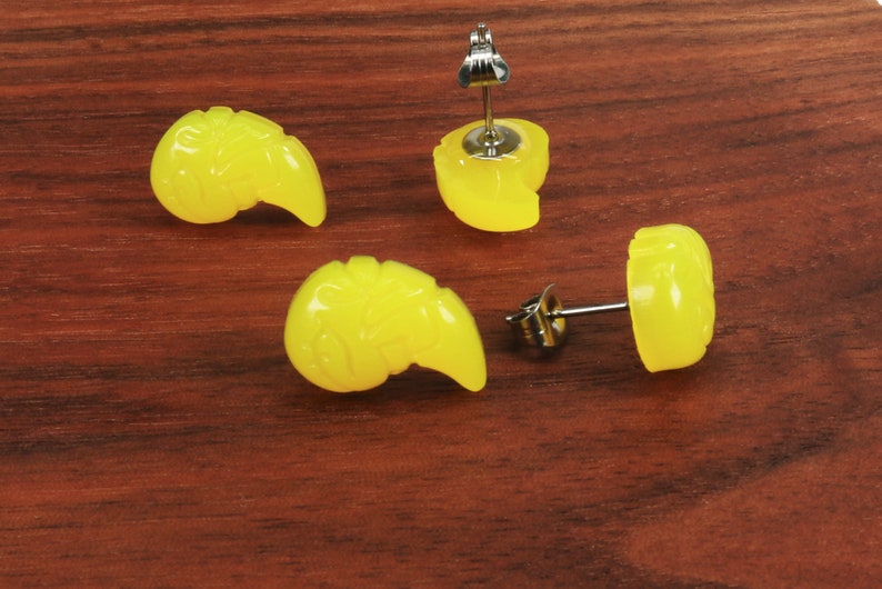May include: Four yellow resin earrings in the shape of a stylized seashell. Two earrings have a post back and two earrings have a clip-on back.