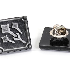 May include: A silver and black enamel pin with a stylized design of three arrows pointing in different directions. The pin has a black backing and a metal pin back.